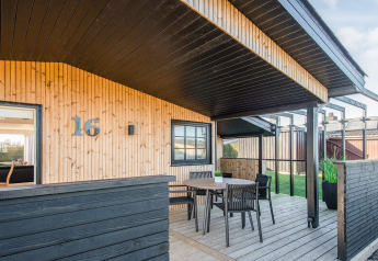 Casa de playa renovada en Dinamarca con terraza de madera techada, mesa y sillas cerca de la entrada 16.
