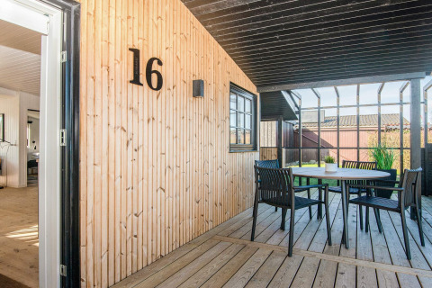 Terrasse couverte d'une maison de plage rénovée au Danemark, mur en bois, numéro 16 et salon de jardin.