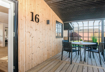 Porche cubierto de casa de playa renovada en Dinamarca con paredes de madera, número 16 y mesa exterior.