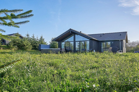 Moderne feriebolig til 8 personer i Aakirkeby, Danmark, omgivet af grøn natur og blå himmel.