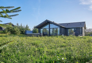 Moderne feriebolig til 8 personer i Aakirkeby, Danmark, omgivet af grøn natur og blå himmel.