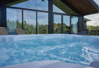 Bubbelend buitenbubbelbad aan een vakantiewoning in Aakirkeby, Denemarken, met ligstoelen en glasgevel.
