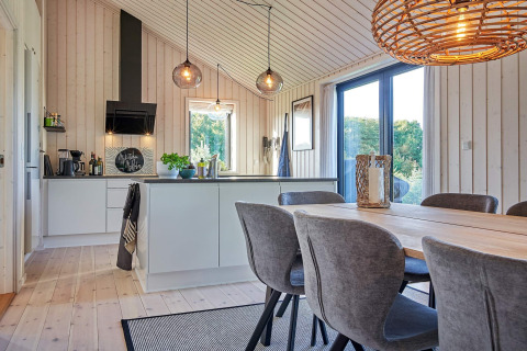 Cocina y comedor modernos con grandes ventanas y paredes de madera en una casa de vacaciones en Aakirkeby, Dinamarca.