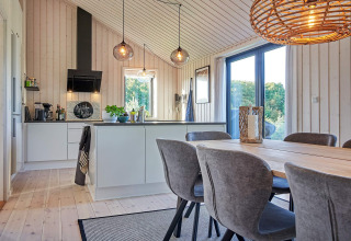 Moderne keuken en eetruimte met grote ramen en houten wanden in een vakantiehuis in Aakirkeby, Denemarken.