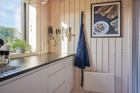 Coin cuisine lumineux dans une maison de vacances à Aakirkeby, Danemark, avec ustensiles, tablier et cadre mural.