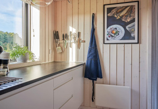 Coin cuisine lumineux dans une maison de vacances à Aakirkeby, Danemark, avec ustensiles, tablier et cadre mural.