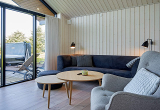 Moderne stue i et sommerhus i Aakirkeby, Danmark, med store vinduer, hjørnesofa og udsigt til terrasse.