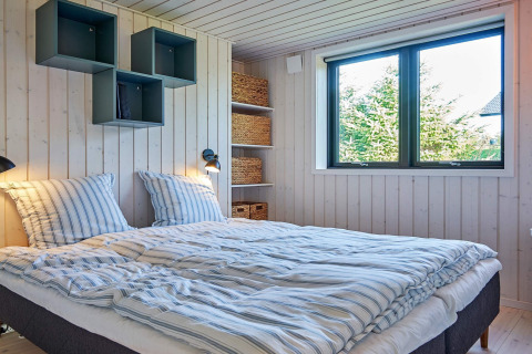 Dormitorio con cama doble, gran ventana y estantes modernos en casa de vacaciones en Aakirkeby, Dinamarca.
