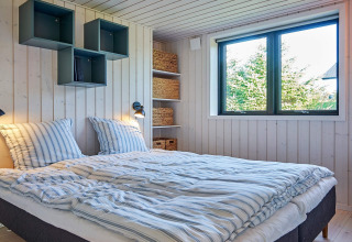 Chambre avec lit double, grande fenêtre et étagères modernes dans une maison de vacances à Aakirkeby.