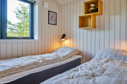 Heldere kamer met twee eenpersoonsbedden, houten wand, raam, wandlamp en decoratieve planken in Deense lodge.
