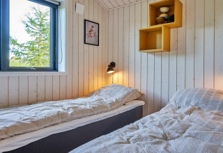 Helles Zimmer mit zwei Einzelbetten, Holzvertäfelung, Fenster, Wandlampe und Dekoregal in dänischer Lodge.