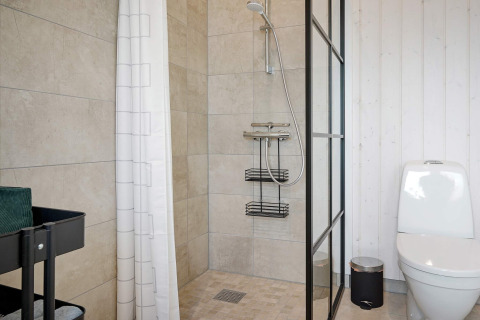 Baño moderno con ducha a ras de suelo, inodoro blanco, cubo y carro de almacenaje en Aakirkeby, Dinamarca.