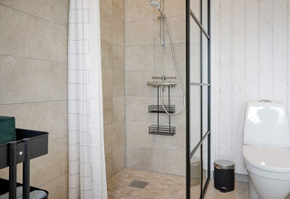 Salle de bain moderne avec douche à l'italienne, toilettes blanches et chariot de rangement à Aakirkeby.