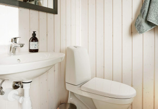 Salle de bain avec lavabo, toilettes blanches et serviette dans maison de vacances 8 personnes à Aakirkeby, Danemark.