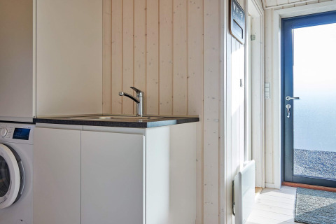Moderne wasruimte met wasmachine, gootsteen en buitendeur in een vakantiehuis in Aakirkeby, Denemarken.