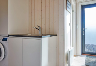Buanderie moderne avec machine à laver, évier et porte extérieure dans un gîte à Aakirkeby, Danemark.