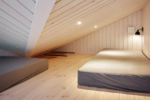Skråloftet soveværelse med to madrasser og minimalistisk indretning i et feriehus i Aakirkeby, Danmark.