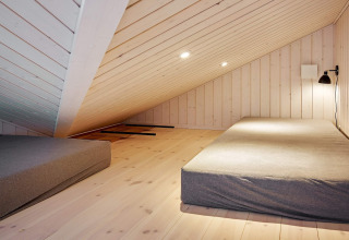 Chambre mansardée avec plafond en bois incliné et deux matelas, décoration minimaliste à Aakirkeby, Danemark.