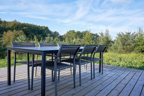 Mesa de comedor exterior y seis sillas en terraza de madera con vista al bosque en casa de vacaciones para 8 en Aakirkeby, Dinamarca.