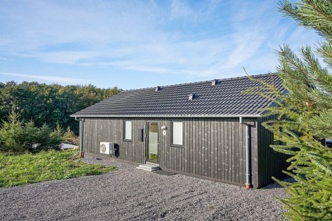 Chalet en bois noir avec tuiles grises entouré de verdure au gîte 8 personnes à Aakirkeby, Danemark.