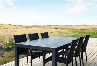 Terrazza con tavolo da pranzo nero e sei sedie, vista su dune e prato a Hjørring, Danimarca.