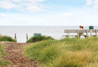 Kvinde sidder på bænk ved stranden med udsigt til havet ved 7 personers feriehus i Hjørring, Danmark.
