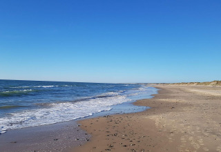 Photo of a peaceful sandy beach with gentle waves and blue sky at a holiday lodge in Hjørring, Denmark.