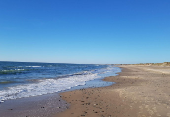 Photo of a peaceful sandy beach with gentle waves and blue sky at a holiday lodge in Hjørring, Denmark.