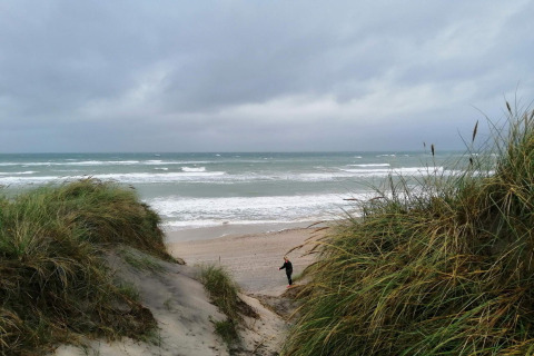Udsigt fra klit ved stranden nær 7 personers feriehus i Hjørring, Danmark, med havbølger og skyer.
