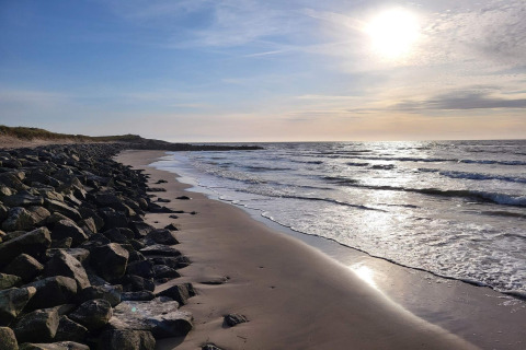 Rotsachtige kust en rustige golven bij zonsondergang in Hjørring, Denemarken, vanaf een vakantiehuis.