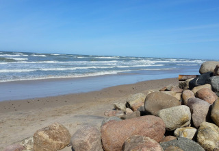 Kustzicht bij 7-persoons vakantiehuis in Hjørring, Denemarken, met stenen en branding op het strand.