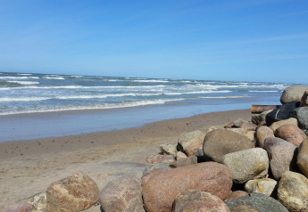 Kustzicht bij 7-persoons vakantiehuis in Hjørring, Denemarken, met stenen en golven op het strand.