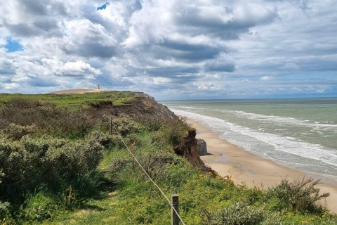 View from 7 person holiday home in Hjørring, Denmark showing cliffs, sandy beach and cloudy sky.