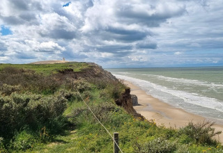 View from 7 person holiday home in Hjørring, Denmark showing cliffs, sandy beach and cloudy sky.