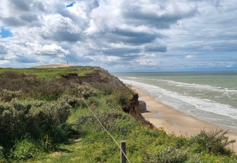 Uitzicht vanaf een vakantiehuis in Hjørring, Denemarken: kliffen, strand en een bewolkte lucht.