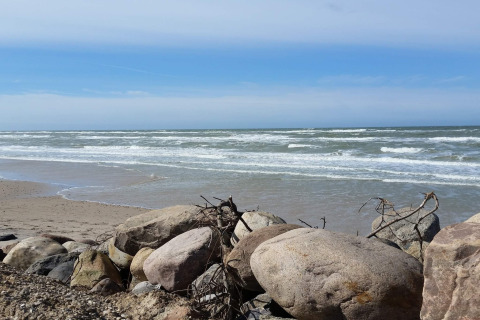 Vista sulla spiaggia e sul mare con grandi rocce in primo piano presso la casa vacanze per 7 persone a Hjørring, Danimarca.