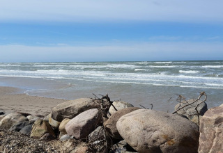 Uitzicht op strand en zee met grote keien op de voorgrond bij het vakantiehuis voor 7 personen in Hjørring, Denemarken.
