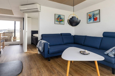 Moderne stue i et feriehus i Hjørring, Danmark med blå sofa, kunst på væggen og udsigt til terrassen.