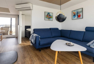 Moderne woonkamer in een vakantiehuis in Hjørring, Denemarken met blauwe zetel, kunst en terraszicht.
