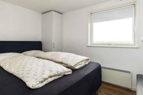 Bedroom with double bed, plain décor, wardrobe and large window in a holiday home in Hjørring, Denmark.