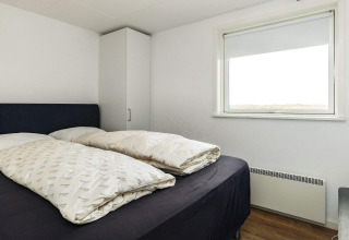 Camera da letto con letto matrimoniale, arredo semplice, armadio e ampia finestra in Hjørring, Danimarca.