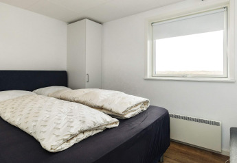 Slaapkamer met tweepersoonsbed, eenvoudige inrichting, kast en groot raam in vakantiehuisje in Hjørring, Denemarken.