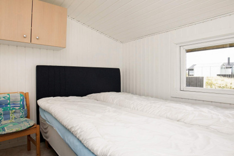 Soveværelse med dobbeltseng, sort sengegavl, stol og vindue i et feriehus i Hjørring, Danmark.