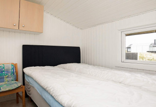 Bedroom with double bed, black headboard, chair and window at a holiday home in Hjørring, Denmark.