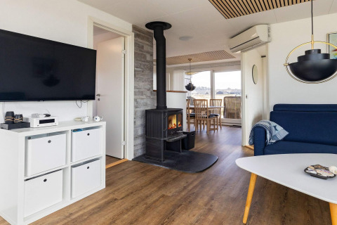 Living room with wood stove, blue sofa, white coffee table and flat-screen TV in Hjørring, Denmark lodge.