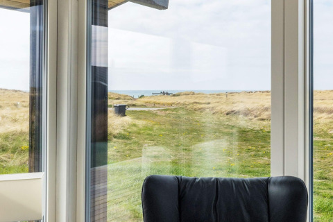Udsigt fra stuen i et sommerhus i Hjørring, Danmark, med havet og klitter synlige gennem vinduet.