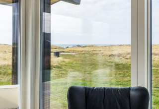 Vista dall'interno di una casa vacanze a Hjørring, Danimarca, con dune e mare visibili dalla finestra.
