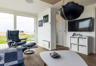 Soggiorno moderno con poltrona, ampia finestra, lampada nera e TV in una casa vacanze a Hjørring, Danimarca.