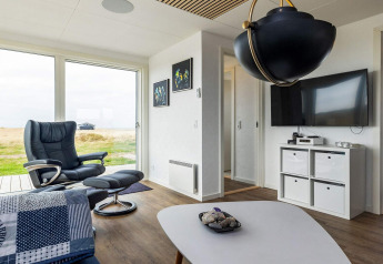 Modernes Wohnzimmer mit Sessel, großem Fenster, schwarzer Lampe und TV in einem Ferienhaus in Hjørring.