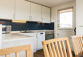 Modern kitchen in a holiday home in Hjørring, Denmark, featuring white cabinets, blue tiles and dining area.